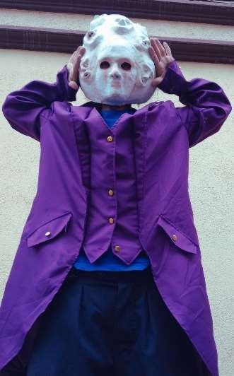 Persona que lleva una máscara blanca con agujeros para los ojos, abrigo morado y orejas que cubren.